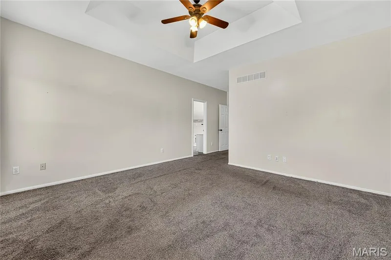 Tray ceiling with a wood-finish ceiling fan, textured carpet flooring, and white painted walls — 934 Annabrook Park Drive, O'Fallon, MO 63366
