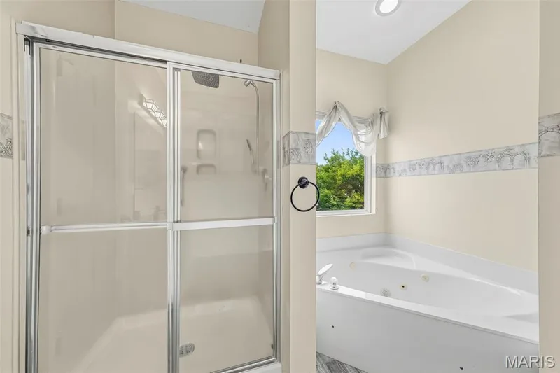 Glass-enclosed shower with showerhead, corner jetted tub, and a window with a valance — 934 Annabrook Park Drive, O'Fallon, MO 63366