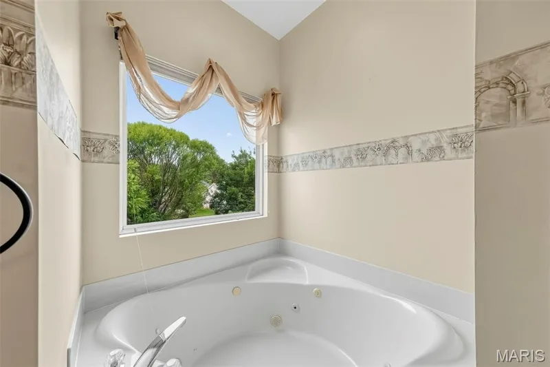 White drop-in jetted tub with chrome fixtures, set against light-toned walls with a decorative border — 934 Annabrook Park Drive, O'Fallon, MO 63366