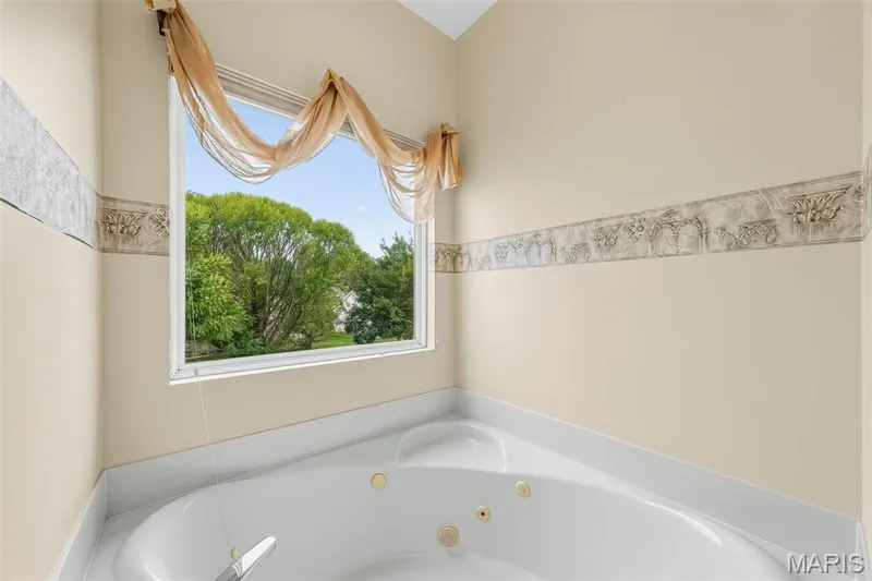 White built-in soaking tub with gold-tone fixtures, set against cream-painted walls with decorative border — 934 Annabrook Park Drive, O'Fallon, MO 63366