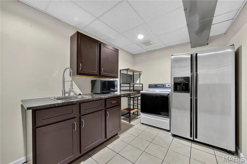 Ceramic tile flooring, dark wood-finish cabinetry, stainless steel sink with gooseneck faucet, drop ceiling with recessed lighting — 934 Annabrook Park Drive, O'Fallon, MO 63366