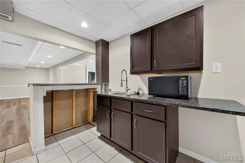 Brown cabinetry and dark speckled countertops define this integrated wet bar with a stainless steel sink and gooseneck faucet — 934 Annabrook Park Drive, O'Fallon, MO 63366