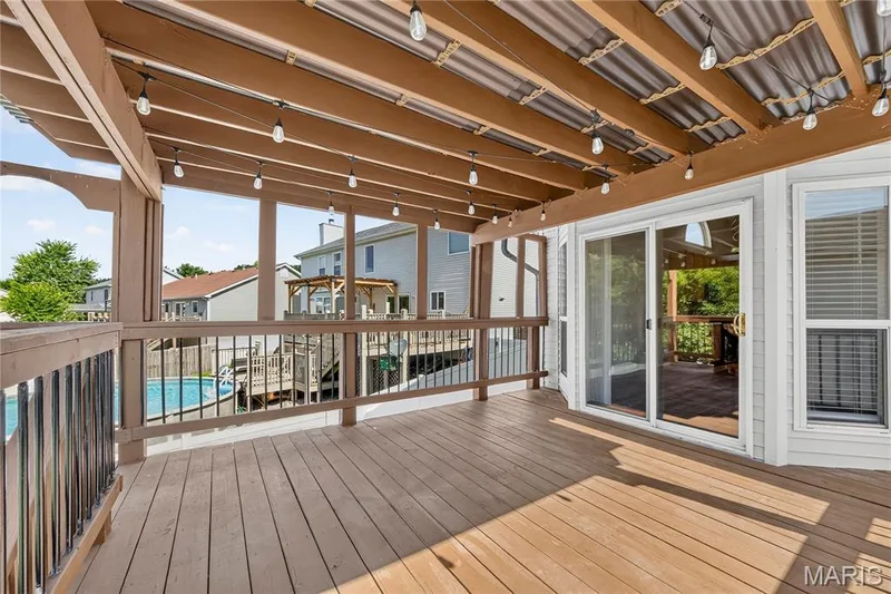 Expansive wood-finish deck with a covered patio, string lighting, and direct access through a sliding glass door — 934 Annabrook Park Drive, O'Fallon, MO 63366