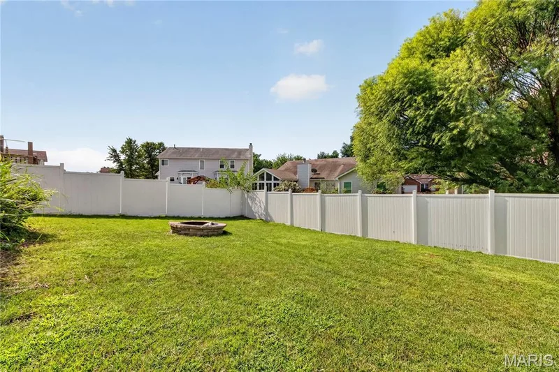 Expansive backyard featuring a manicured lawn, stone fire pit, and white privacy fencing — 934 Annabrook Park Drive, O'Fallon, MO 63366