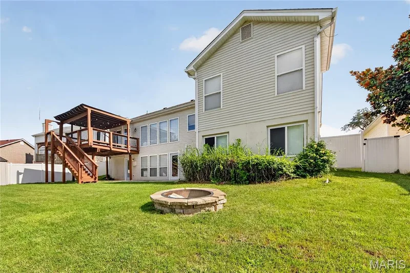 Expansive backyard featuring a manicured lawn, a built-in stone fire pit, and a multi-level wooden deck with a pergola — 934 Annabrook Park Drive, O'Fallon, MO 63366