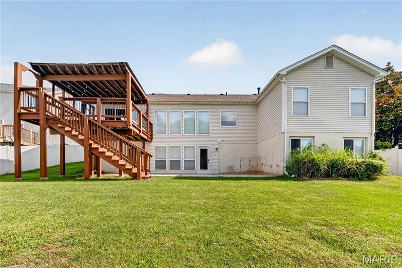 Expansive grassy yard with a multi-level wood deck featuring a covered upper level and direct exterior access — 934 Annabrook Park Drive, O'Fallon, MO 63366
