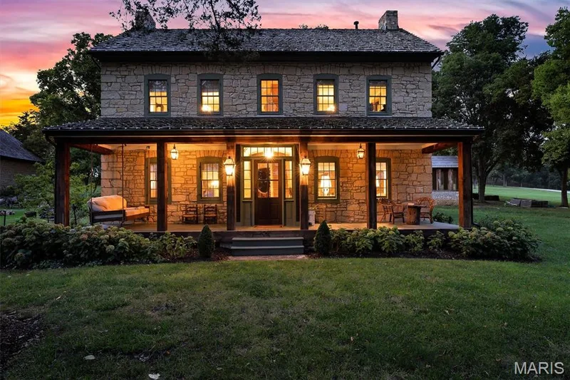 Stone exterior with a covered front porch featuring exposed wood beams and columns, a dark entry door, and multiple windows with dark trim — 2275 Highway F #LOT 1, Defiance, MO 63341