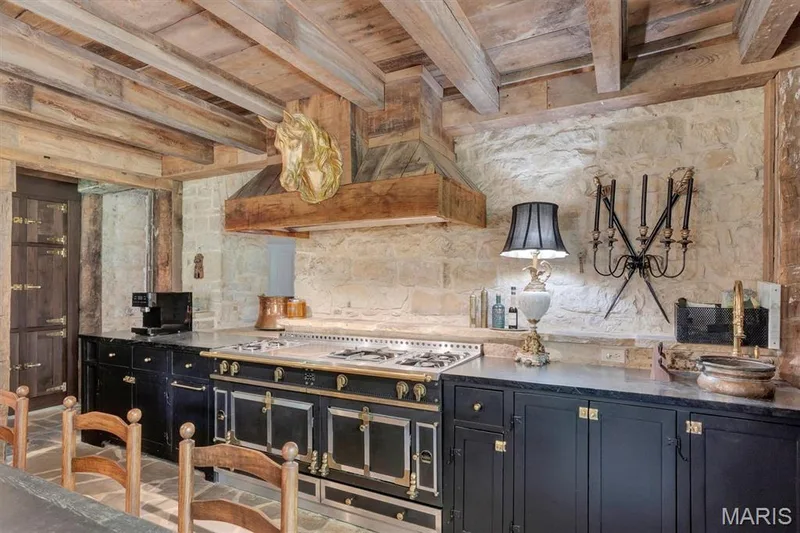 Chef's kitchen featuring an upscale European La Cornue Range with stone  countertops, custom cabinetry with brass hardware, exposed wooden ceiling beams, and a marble tile backsplash with a decor — 2275 Highway F #LOT 1, Defiance, MO 63341