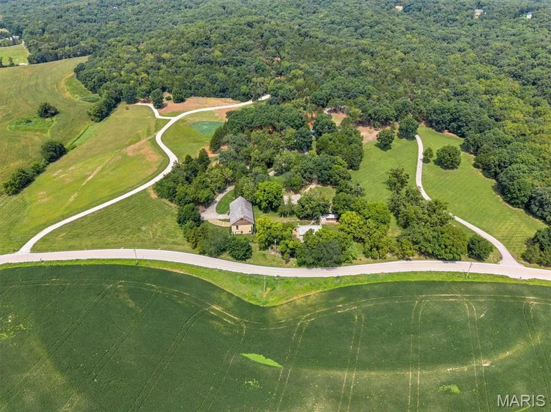 Expansive property featuring a central residence, winding paved driveways, a large wooded area, and surrounding green fields — 2275 Highway F #LOT 1, Defiance, MO 63341