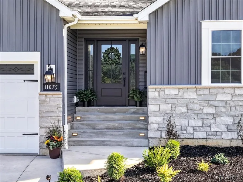 A covered entry, full-view door with sidelights and illuminated steps create a polished first impression. — 11075 Village Drive, Foristell, MO 63348