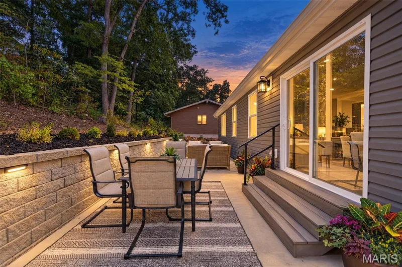 Expansive patio featuring a stone retaining wall with integrated lighting, wood-finish steps, and sliding glass doors — 11075 Village Drive, Foristell, MO 63348