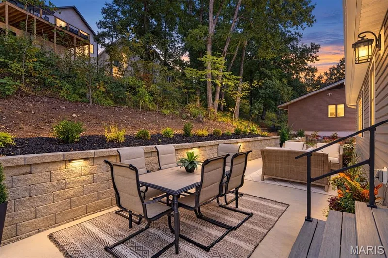 Expansive outdoor patio featuring concrete paving and a stone-block retaining wall with integrated lighting — 11075 Village Drive, Foristell, MO 63348
