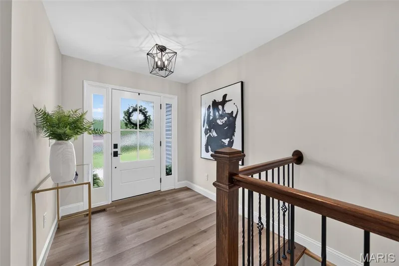 A welcoming foyer features wide-plank flooring, statement lighting and a handsome wood-and-iron railing. — 11075 Village Drive, Foristell, MO 63348