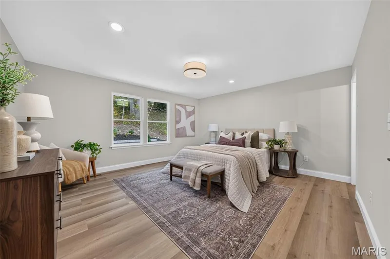 The spacious primary suite features a large double window framing picturesque patio and landscape views. — 11075 Village Drive, Foristell, MO 63348