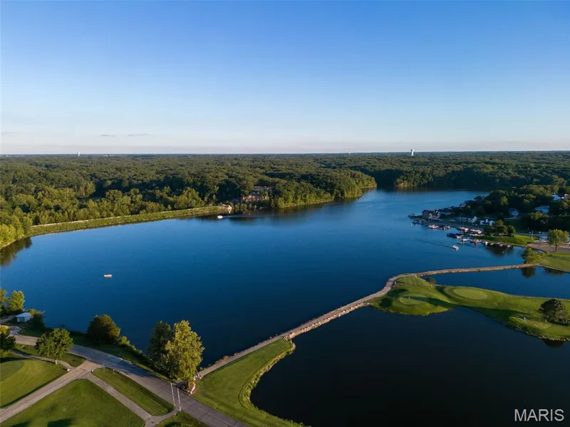Expansive lake with surrounding mature trees, a stone bridge, and a golf course — 11075 Village Drive, Foristell, MO 63348