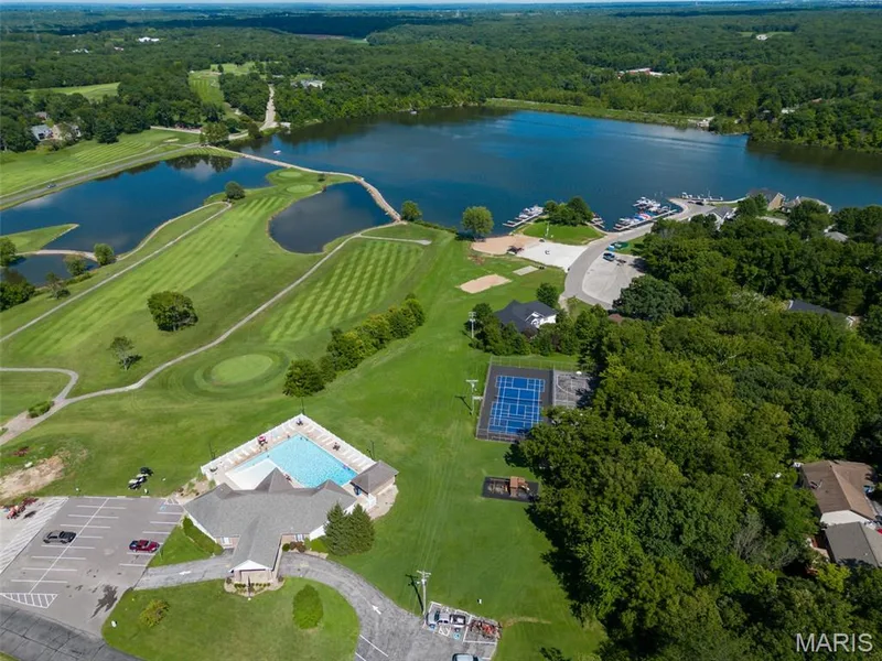 Expansive lake with a marina, golf course with manicured greens, swimming pool, tennis courts, and abundant tree cover — 11075 Village Drive, Foristell, MO 63348
