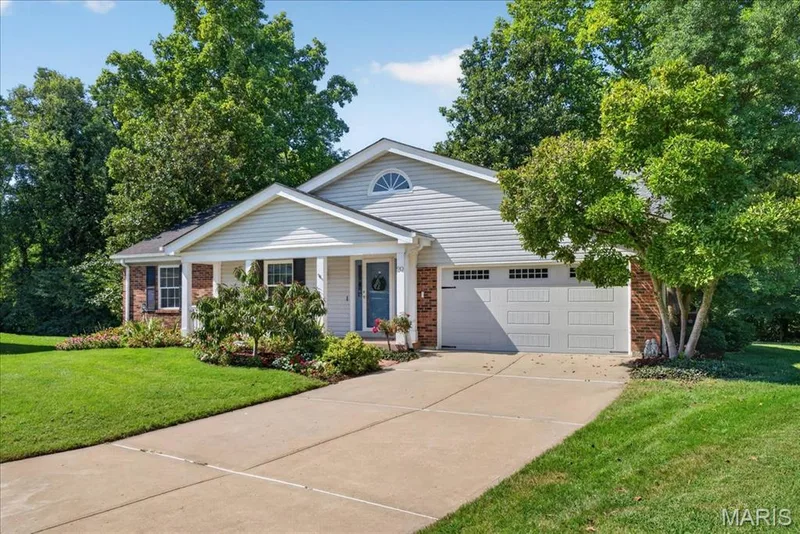 Light-colored siding exterior with brick accents, an arched window detail, a covered front entry, and an attached garage with panel detailing — 20 Ardennais Road, St Peters, MO 63376
