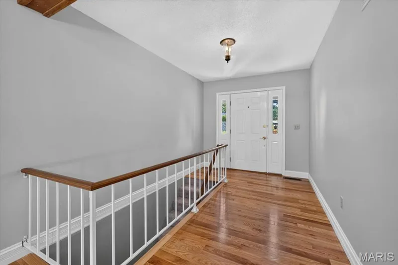 Wood-finish flooring, white entry door with clear glass sidelights, white door trim, and a white spindle railing with wood-finish handrail — 20 Ardennais Road, St Peters, MO 63376