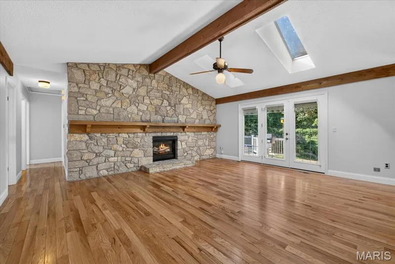 Vaulted ceiling with exposed wood beams, stone-clad fireplace, wood-finish flooring, and double glass doors — 20 Ardennais Road, St Peters, MO 63376