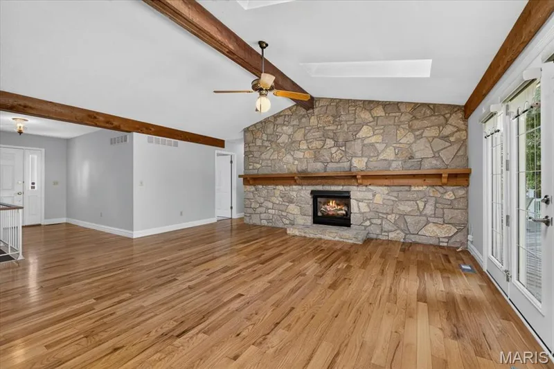 Vaulted ceiling with exposed wood beams, stone fireplace with wood mantel, hardwood flooring, and double French doors — 20 Ardennais Road, St Peters, MO 63376
