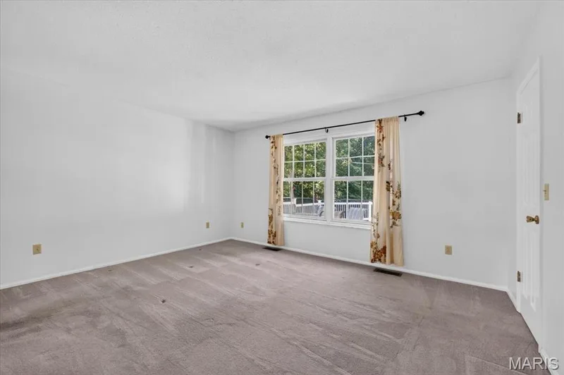 Primary- Carpeted flooring with white wall finishes, a double window with a dark-finish curtain rod, and a white interior door with brass-finish hardware — 20 Ardennais Road, St Peters, MO 63376