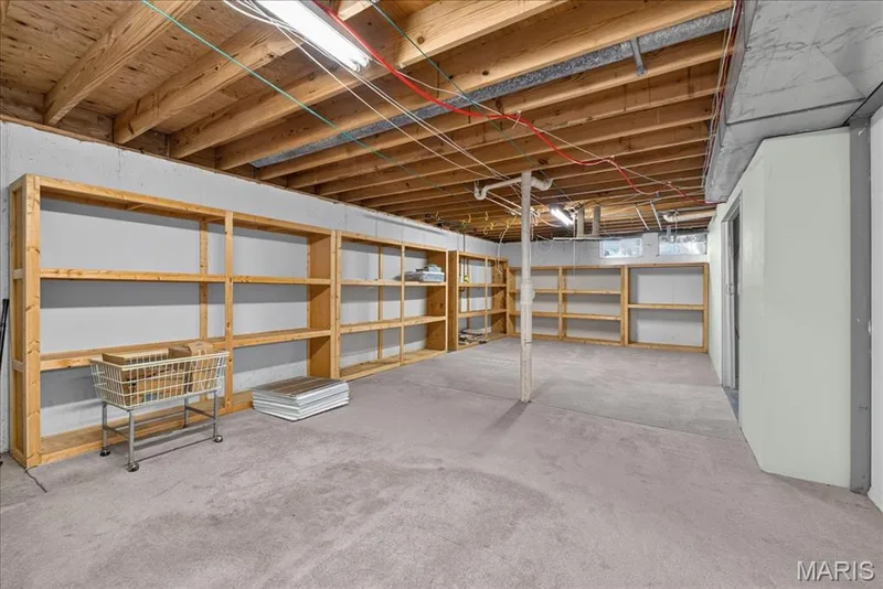 Spacious lower level featuring exposed ceiling joists, concrete foundation walls, built-in wooden shelving, and a finished floor — 20 Ardennais Road, St Peters, MO 63376