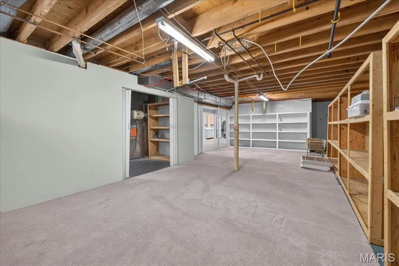 Finished basement space featuring carpeting, exposed wood ceiling joists, overhead fluorescent lighting, and built-in shelving units — 20 Ardennais Road, St Peters, MO 63376