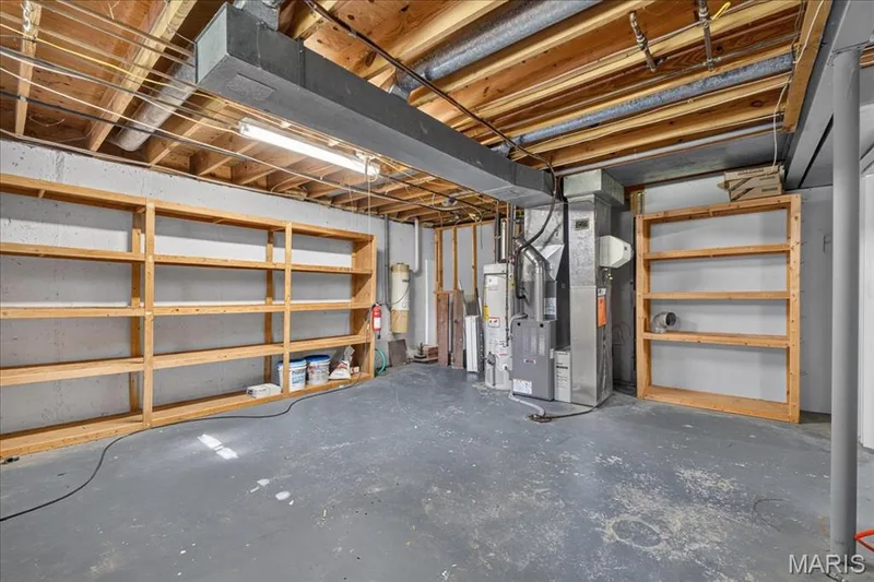 Unfinished basement with exposed ceiling joists, concrete foundation walls, built-in wooden shelving, and a painted concrete floor — 20 Ardennais Road, St Peters, MO 63376