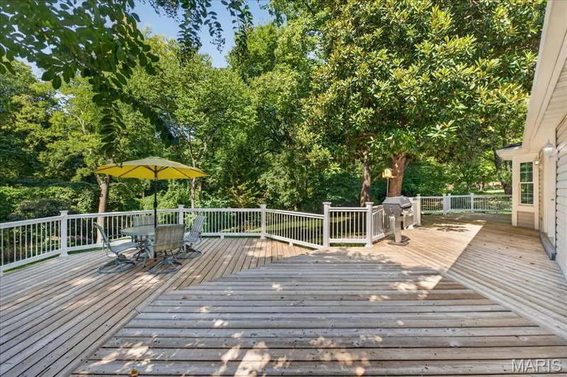 Expansive wood deck with white railings, surrounded by mature trees, featuring a bay window — 20 Ardennais Road, St Peters, MO 63376