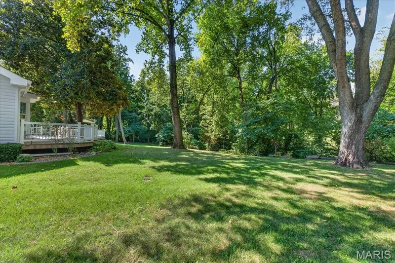 Expansive lawn with mature trees and a wood deck featuring white railings — 20 Ardennais Road, St Peters, MO 63376