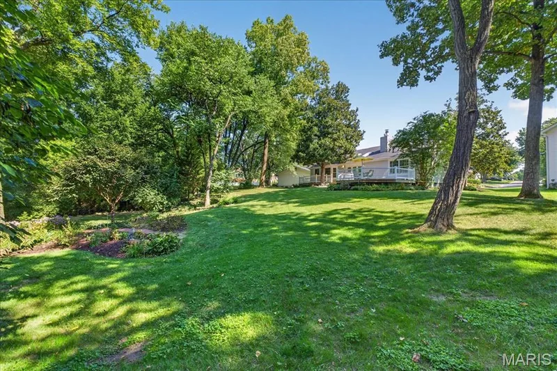 Expansive green lawn with mature trees, a raised garden bed, and a property with a spacious deck — 20 Ardennais Road, St Peters, MO 63376