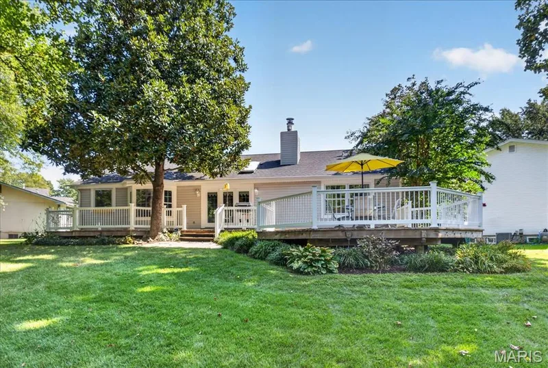 Expansive rear deck with white railings, a stone patio, and mature trees surrounding a lush lawn — 20 Ardennais Road, St Peters, MO 63376