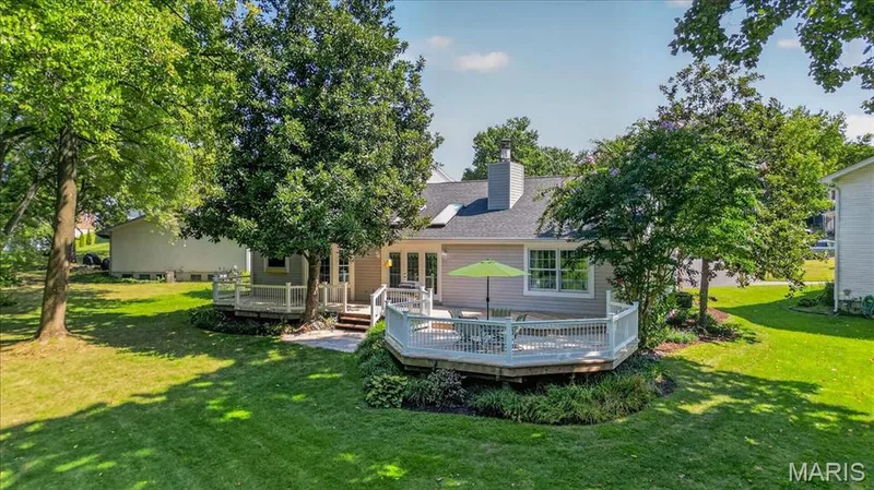 Expansive backyard featuring a manicured lawn, mature trees, multi-level deck with white railings, and a stone patio — 20 Ardennais Road, St Peters, MO 63376
