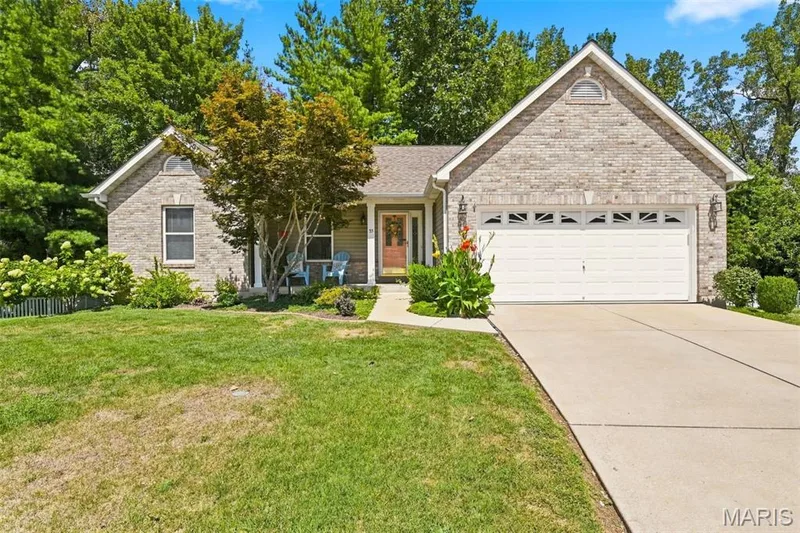 Brick exterior with an attached garage, featuring a concrete driveway and mature trees — 55 Treeshade Court, St Peters, MO 63376