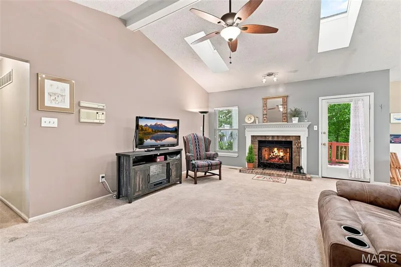 Vaulted ceiling with skylights and ceiling fan, brick fireplace with mantel, and light-toned carpeting — 55 Treeshade Court, St Peters, MO 63376