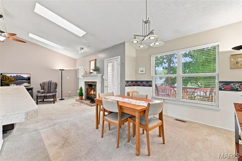 Vaulted ceiling with skylights, wood-burning fireplace with white mantel, built-in breakfast bar, white framed window with blinds, and ceiling fan — 55 Treeshade Court, St Peters, MO 63376