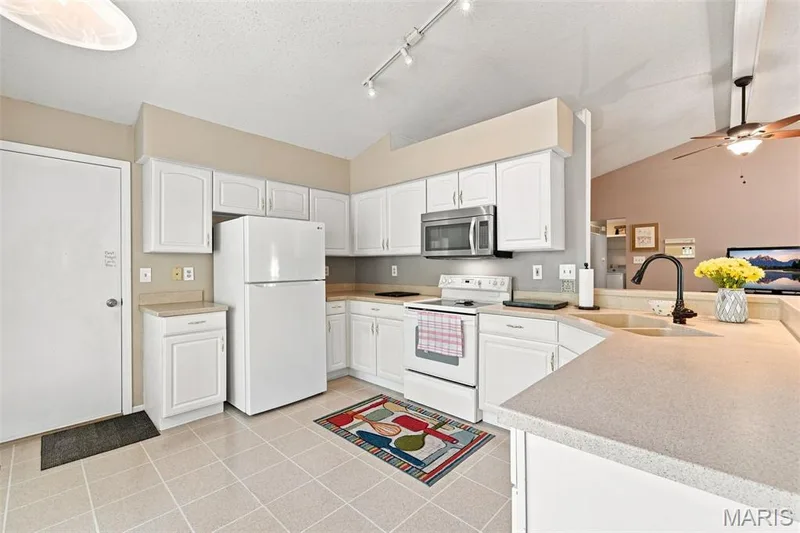 Kitchen featuring white cabinetry, light-toned countertops, a stainless steel microwave, a white range, and tiled flooring — 55 Treeshade Court, St Peters, MO 63376