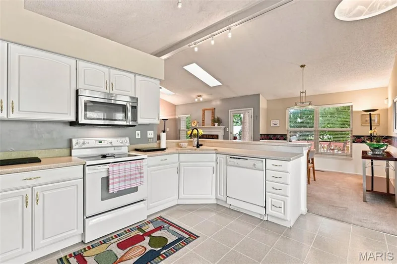 Kitchen featuring white cabinetry, light-toned countertops, a stainless steel microwave, and tile flooring — 55 Treeshade Court, St Peters, MO 63376
