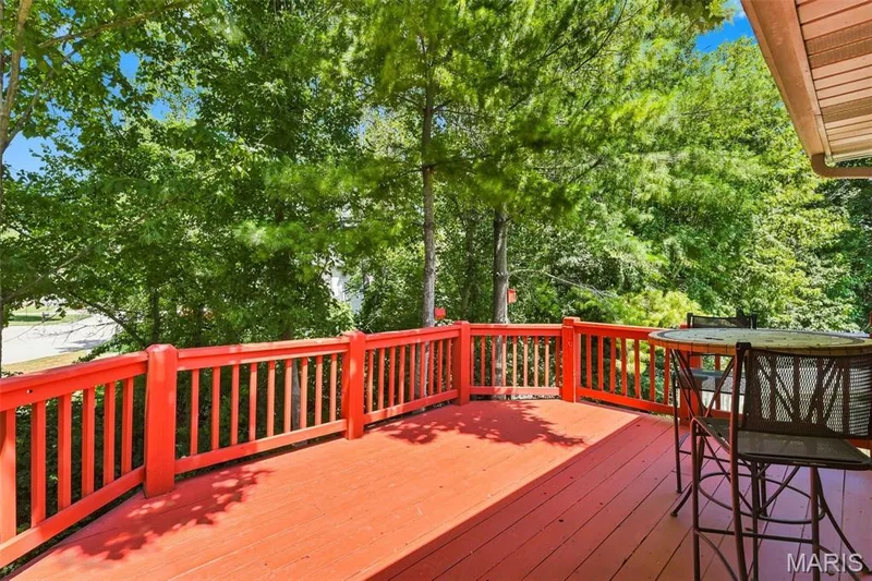 Red-stained wood deck featuring a matching railing and natural tree canopy — 55 Treeshade Court, St Peters, MO 63376