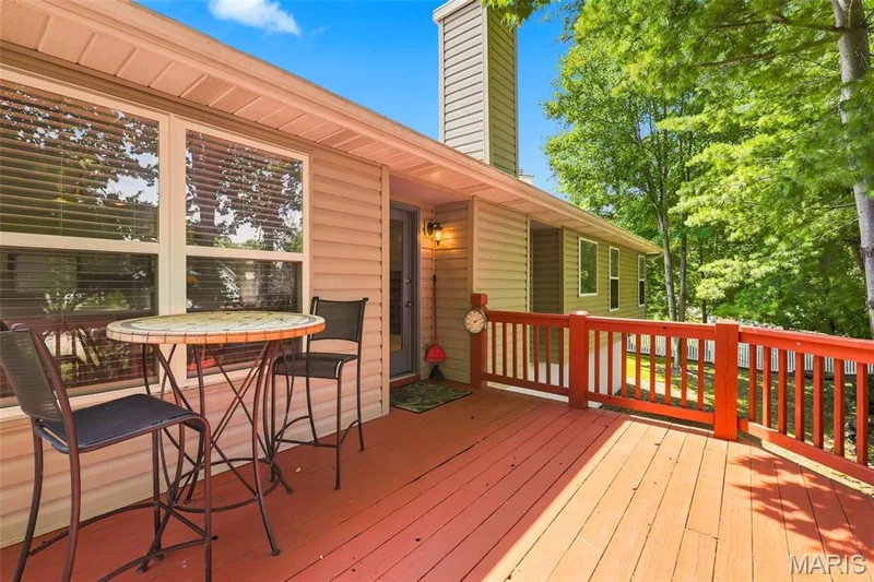 Expansive outdoor deck with red-stained wood flooring and matching railings, featuring vinyl siding and multiple windows — 55 Treeshade Court, St Peters, MO 63376