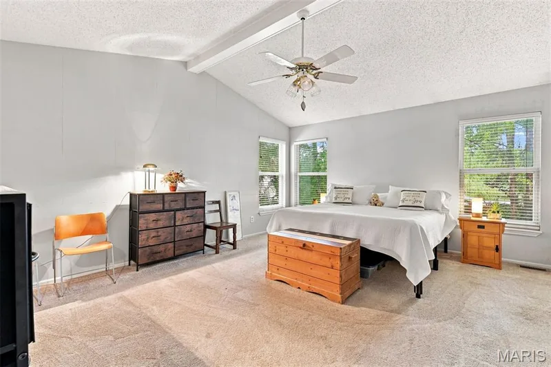 Vaulted ceiling with exposed beam, multiple windows providing natural light, ceiling fan with integrated lighting, and neutral-toned wall paint — 55 Treeshade Court, St Peters, MO 63376