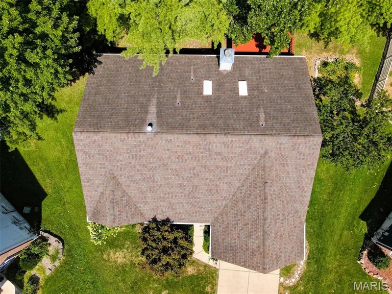 Gabled roofline with asphalt shingles, chimney, two skylights, and established perimeter landscaping — 55 Treeshade Court, St Peters, MO 63376