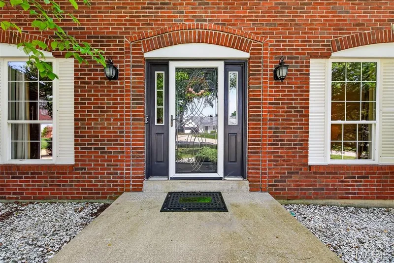 Brick facade, arched entryway, decorative front door with sidelights, dual exterior wall sconces, white shuttered windows — 10 Docs Ct., St Charles, MO 63303
