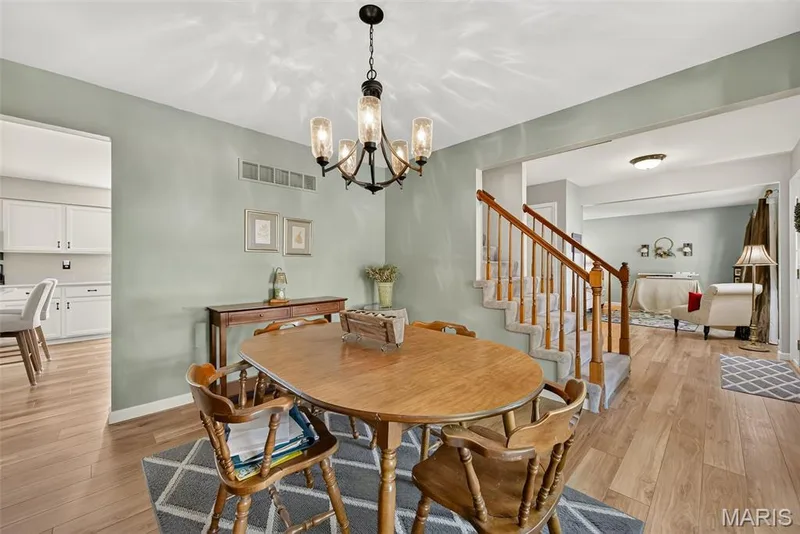 Open-concept living space featuring wood-finish flooring, a contemporary chandelier, and a carpeted staircase with wood banister — 10 Docs Ct., St Charles, MO 63303