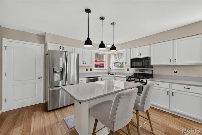 Kitchen featuring white cabinetry, stainless steel appliances, a center island with countertop seating, wood-finish flooring, and pendant lighting — 10 Docs Ct., St Charles, MO 63303