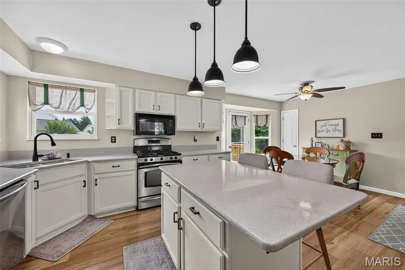 White cabinetry with black hardware, stainless steel appliances, wood-finish flooring, central island with seating, and a bay window — 10 Docs Ct., St Charles, MO 63303