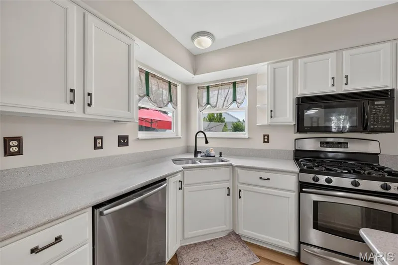 White cabinetry with black hardware, stainless steel appliances, speckled countertops, and an undermount sink with a black faucet — 10 Docs Ct., St Charles, MO 63303