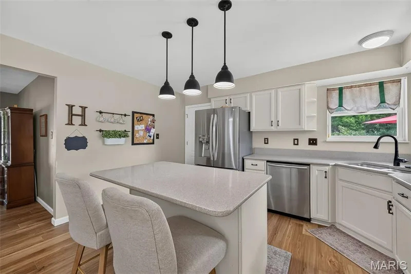 Kitchen featuring a center island with seating, white cabinetry, light countertops, stainless steel appliances, and wood-finish flooring — 10 Docs Ct., St Charles, MO 63303