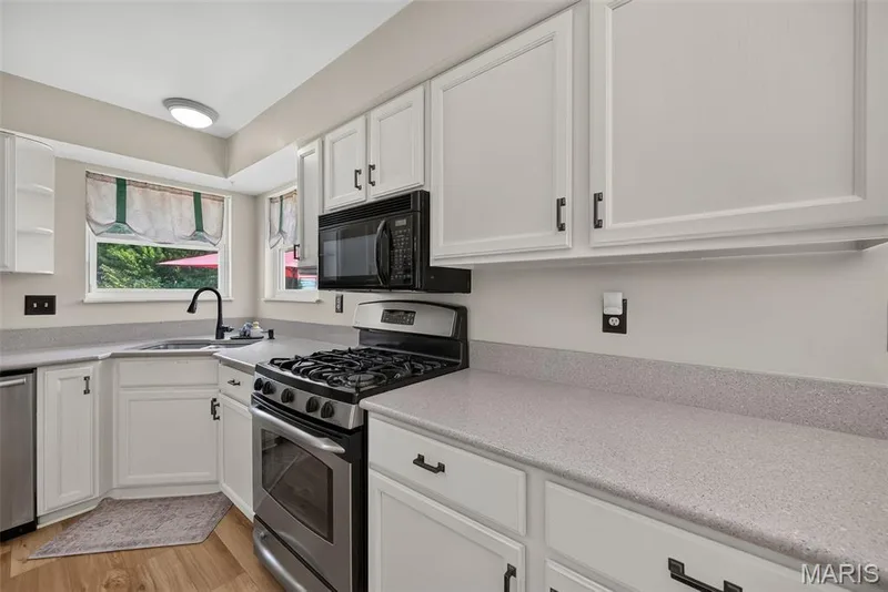 White cabinetry with dark hardware, speckled countertops, stainless steel range, and built-in microwave — 10 Docs Ct., St Charles, MO 63303