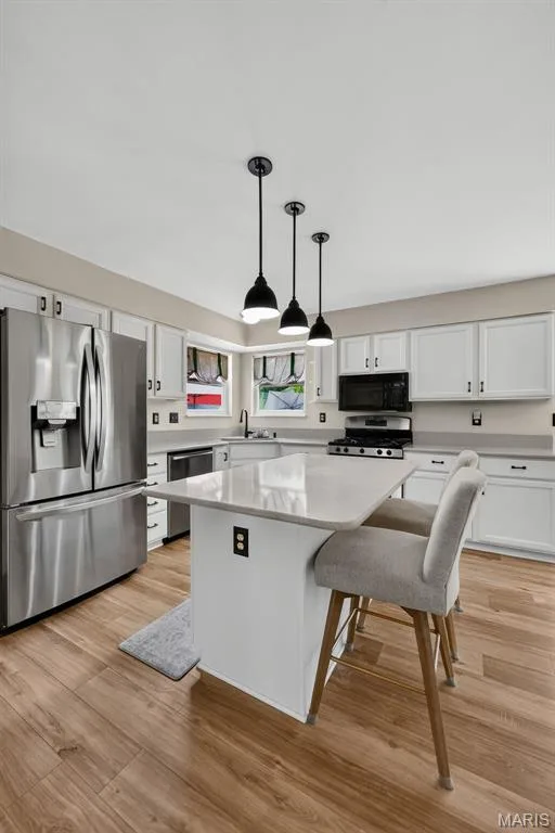 Kitchen featuring wood-finish flooring, white cabinetry, a center island with light-toned countertops, and stainless steel appliances — 10 Docs Ct., St Charles, MO 63303